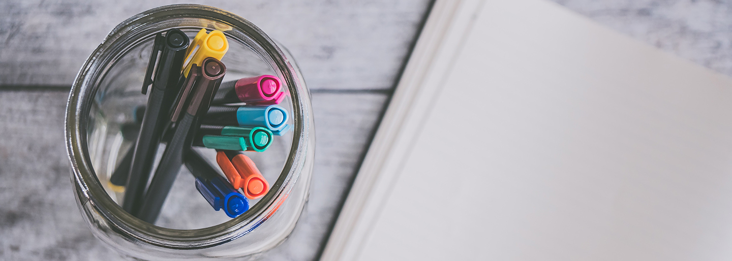 markers in a container and notebook in background